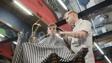 从底部看。 理发店有客户小孩的理发师男。 理发店里用修剪机理发。 可爱的孩子